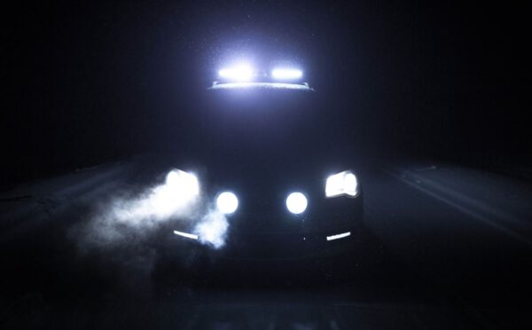 Een auto in rijdt snachts door het donker met mistlampen boven en onder de auto aan.